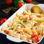 Baked feta pasta in a white oval dish with a gold serving spoon, garnished with fresh parsley and surrounded by cherry tomatoes on a dark rustic background.