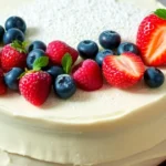 A fluffy vanilla cake with buttercream frosting and fresh berries, served on a white plate with a fork beside it.