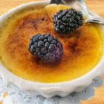 A close-up of individual mini crème brûlée cheesecakes topped with caramelized sugar and fresh berries on a white plate.