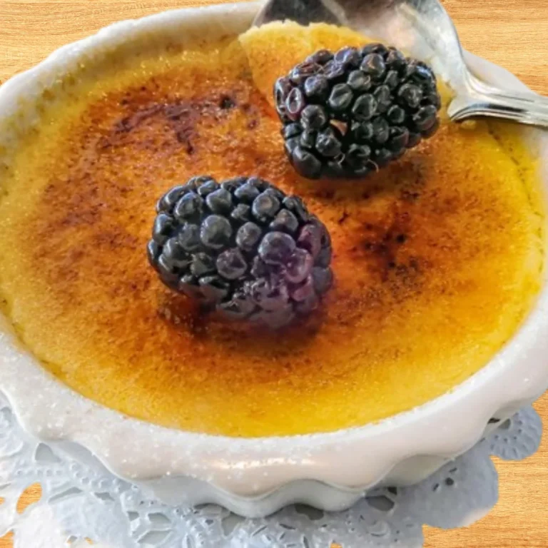 A close-up of individual mini crème brûlée cheesecakes topped with caramelized sugar and fresh berries on a white plate.