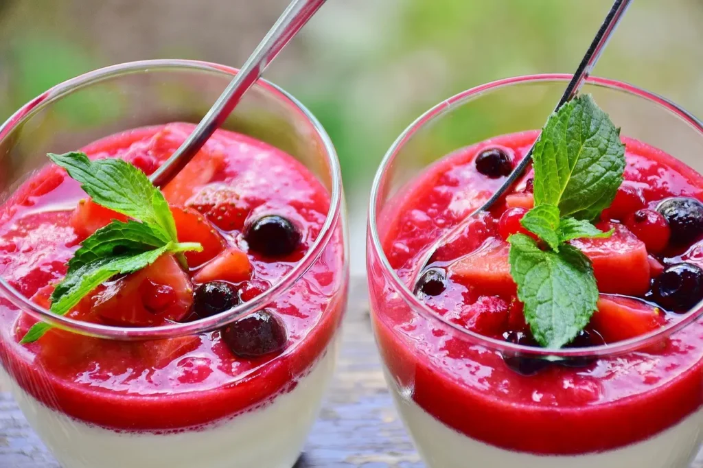 Two glasses filled with panna cotta and topped with berry compote and mint sprigs.