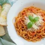 A bowl of creamy tomato pasta topped with fresh basil and Parmesan, served with garlic bread on the side.