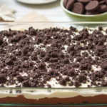 A delicious Oreo dirt cake with layers of crushed Oreos, vanilla pudding, and whipped topping, garnished with extra Oreo crumbs, served in a 9x13-inch dish on a kitchen table.