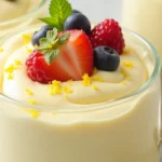 A creamy serving of Philadelphia lemon cheesecake mousse topped with fresh lemon zest, mint leaves, and berries, served in a clear glass cup.